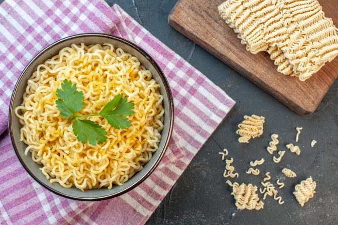 widok-z-gory-azjatycki-makaron-ramen-w-misce-na-rozowym-bialym-obrusie-w-kratke-surowy-makaron-ramen-na-desce-krojenia-na-ciemnym-tle zupka chińska