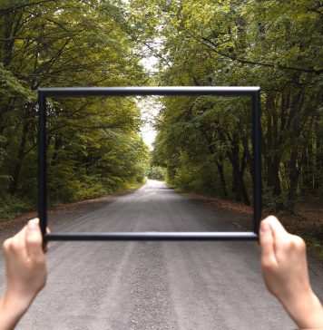 Osoba stojąca na drodze, trzymająca przed sobą pustą ramkę