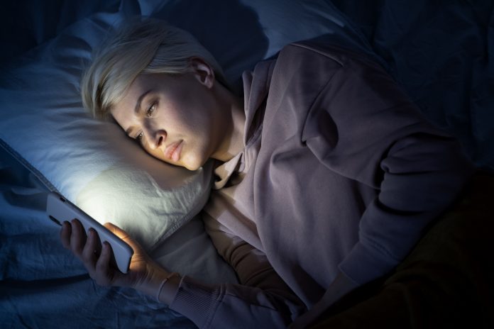 Kobieta leżąca w łóżku i korzystająca z telefonu