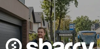 Sharry na tle podróżnik z lekkim uśmiechem idzie ulicą w kierunku przystanku autobusów międzynarodowych, ciągnąc za sobą niewielką walizkę