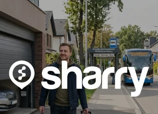Sharry na tle podróżnik z lekkim uśmiechem idzie ulicą w kierunku przystanku autobusów międzynarodowych, ciągnąc za sobą niewielką walizkę